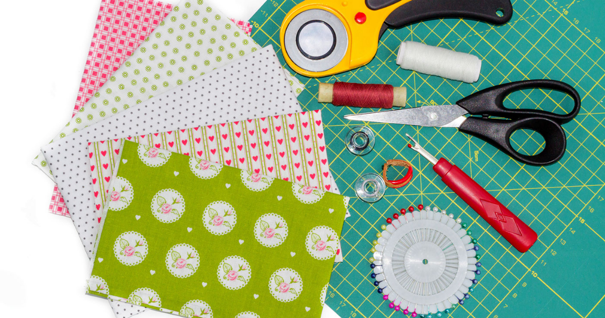 Different quilting supplies lay flat on a table. Shown on screen is 5 fabrics of different colors, scissors, thread, and more