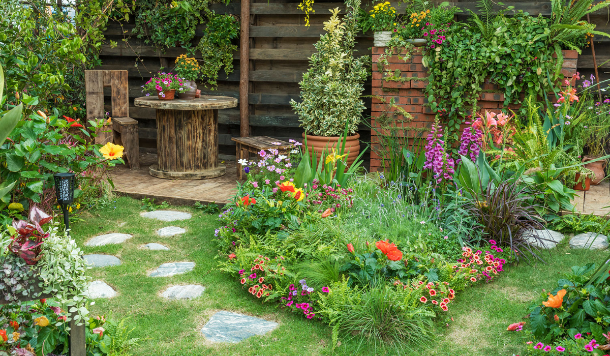 A beautiful garden with a stone pathway between two shrubs with colorful flowers inside of them