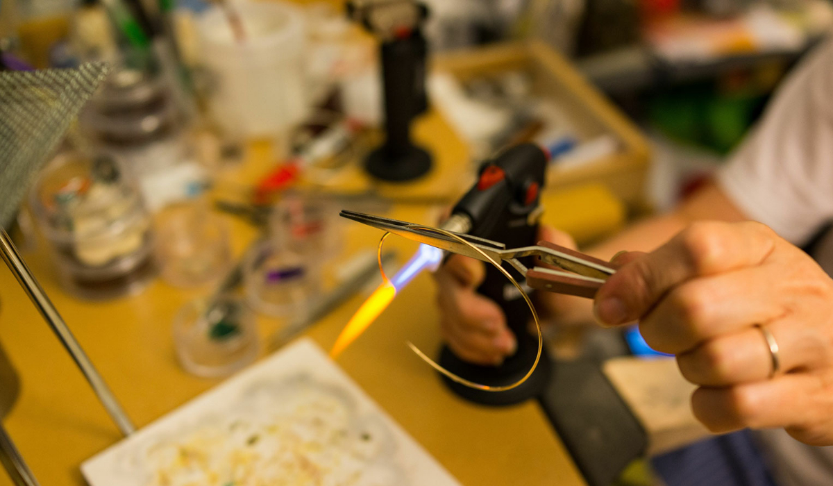 A hand holding a soldering gun pointing at the end of an open braclet is controlling an open flame