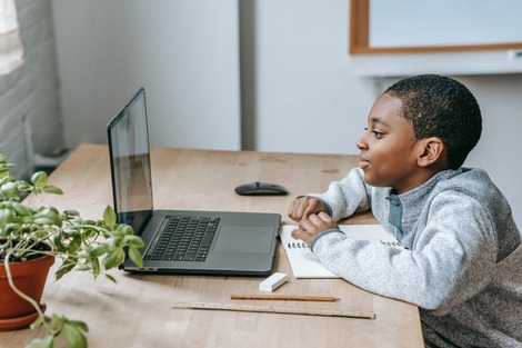 A young boy sits in front of a laptop. He's learning. Teaching kids how to draw can strengthen their learning skills.