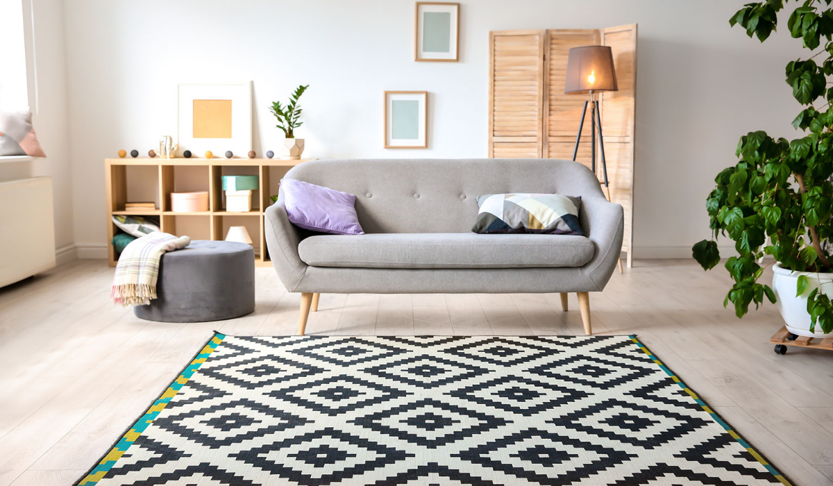 A rug lays in the middle of a room with a sofa above it.