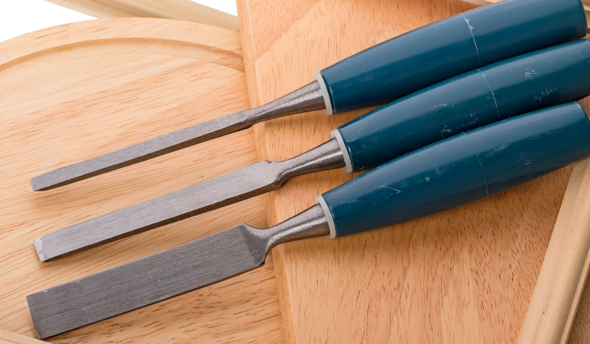 Three chisels with blue handles are laid out on two pieces of wood with a textured stripe along the edges